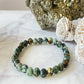 Beads of African Turquoise, a beautiful green, black, and brown stone, made into a bracelet, sitting next to Pyrite and Selenite.